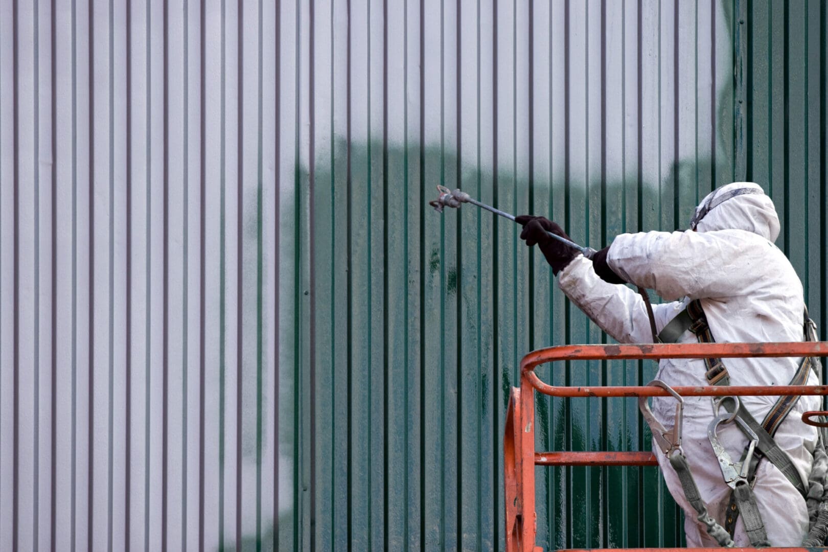 A commercial painter on an industrial lift spray painting a steel exterior wall or duct.